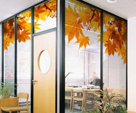 Oficina con paneles de cristal decorados con hojas de otoño y una puerta circular.